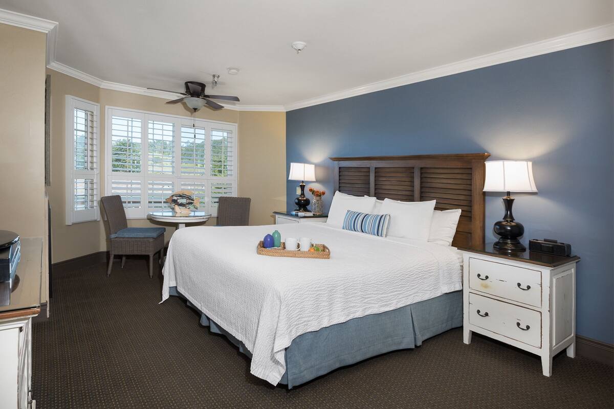 A hotel room with a large bed, a desk, and a chair. There are two nightstands with lamps and a ceiling fan.