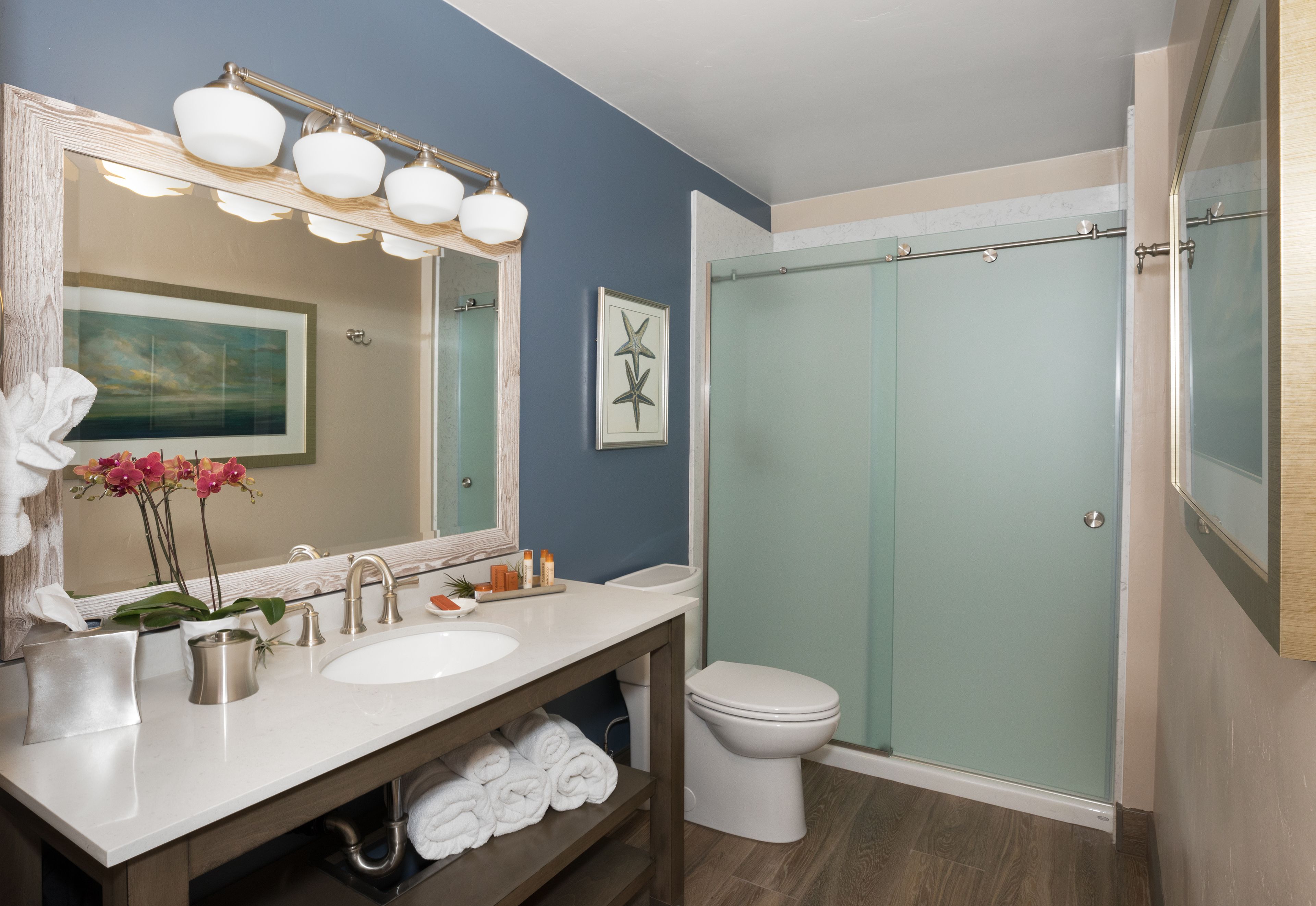 A bathroom with a white sink, a large mirror with lights, a shower with frosted glass doors, and a toilet.