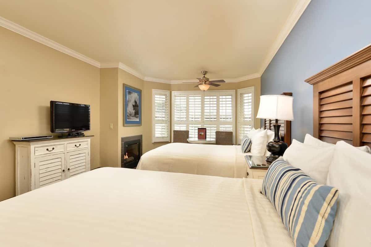 A hotel room with two beds, a television, a fireplace, and a window with shutters.