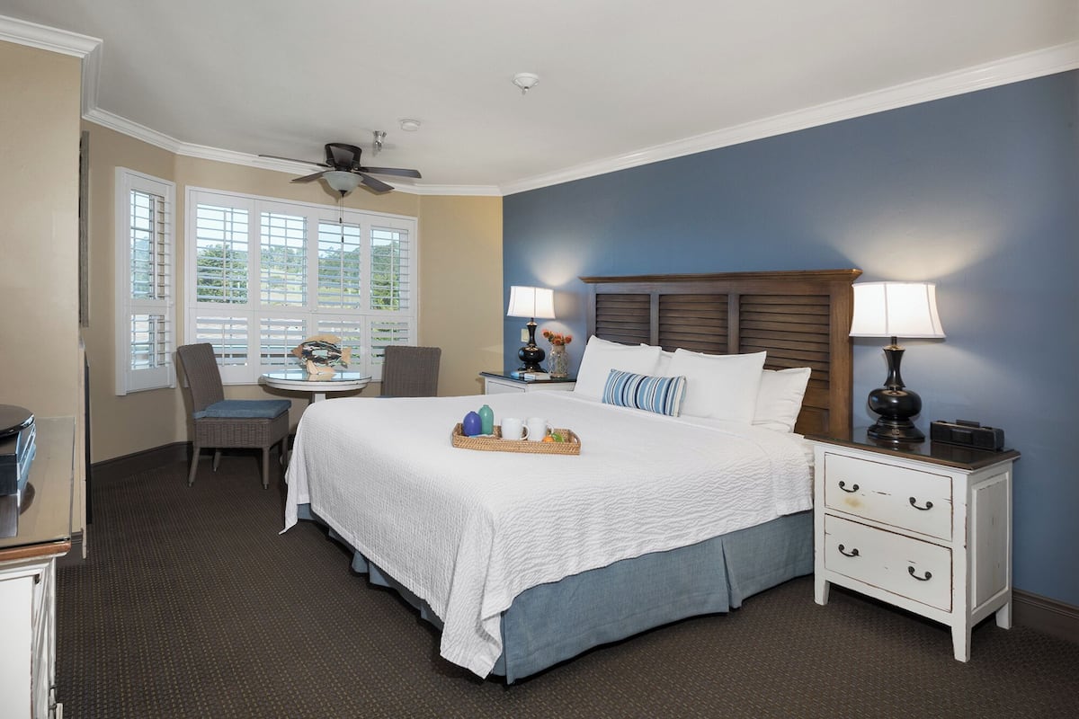 A hotel room with a bed, two bedside tables, a chair, a small table, and a ceiling fan.