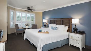 A hotel room with a bed, two bedside tables, a chair, a small table, and a ceiling fan.