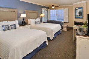 A hotel room with two beds, a desk, a chair, and a television.