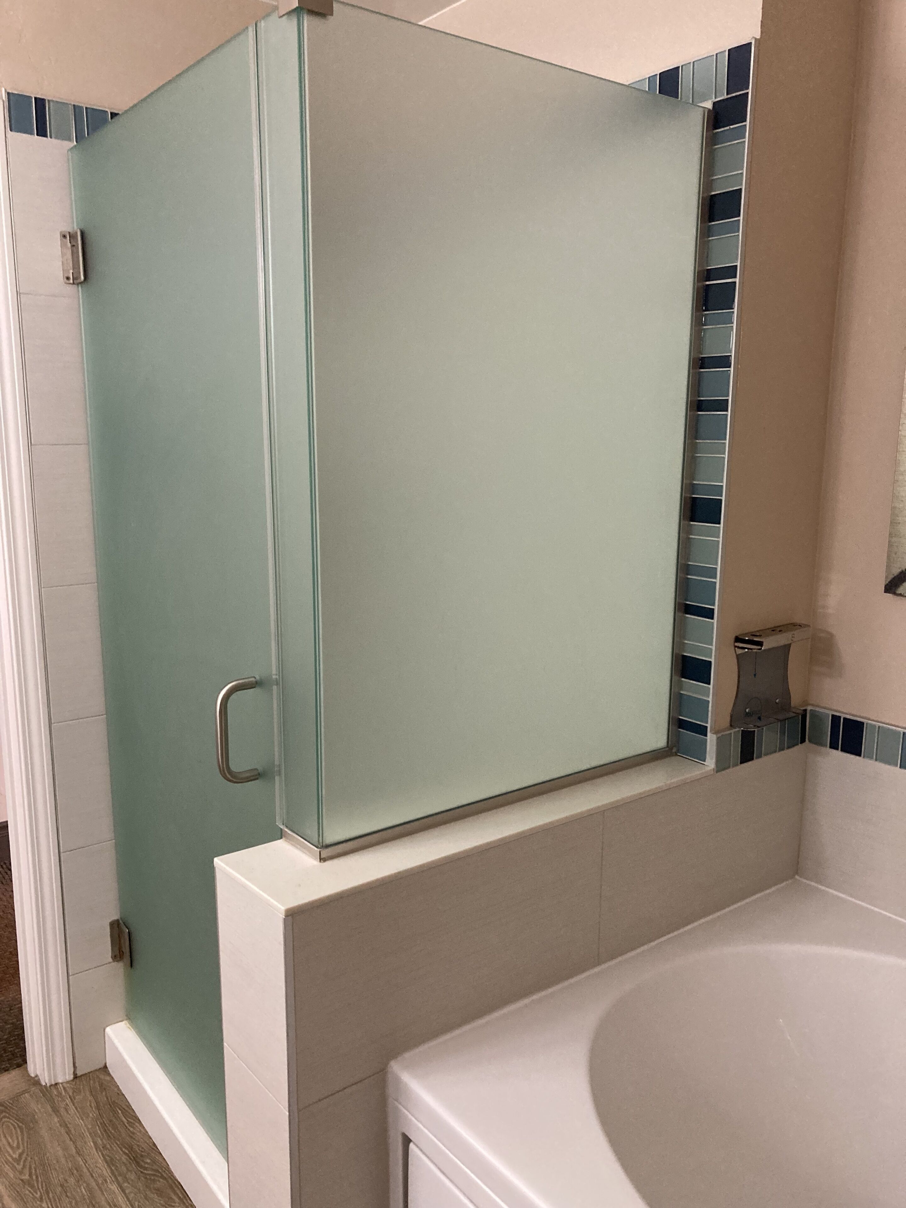 A bathroom with a glass shower enclosure, a white bathtub, and blue-tiled walls.
