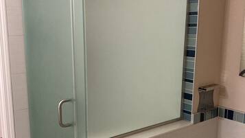 A bathroom with a glass shower enclosure, a white bathtub, and blue-tiled walls.