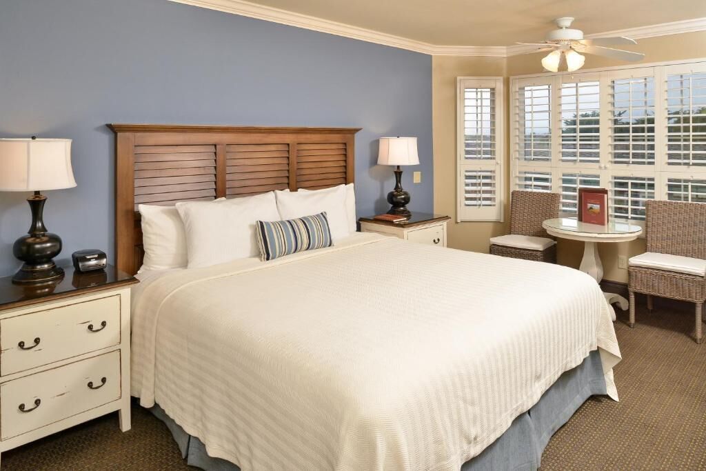 A neatly arranged bedroom with a large bed, bedside lamps, a small table, and a chair.