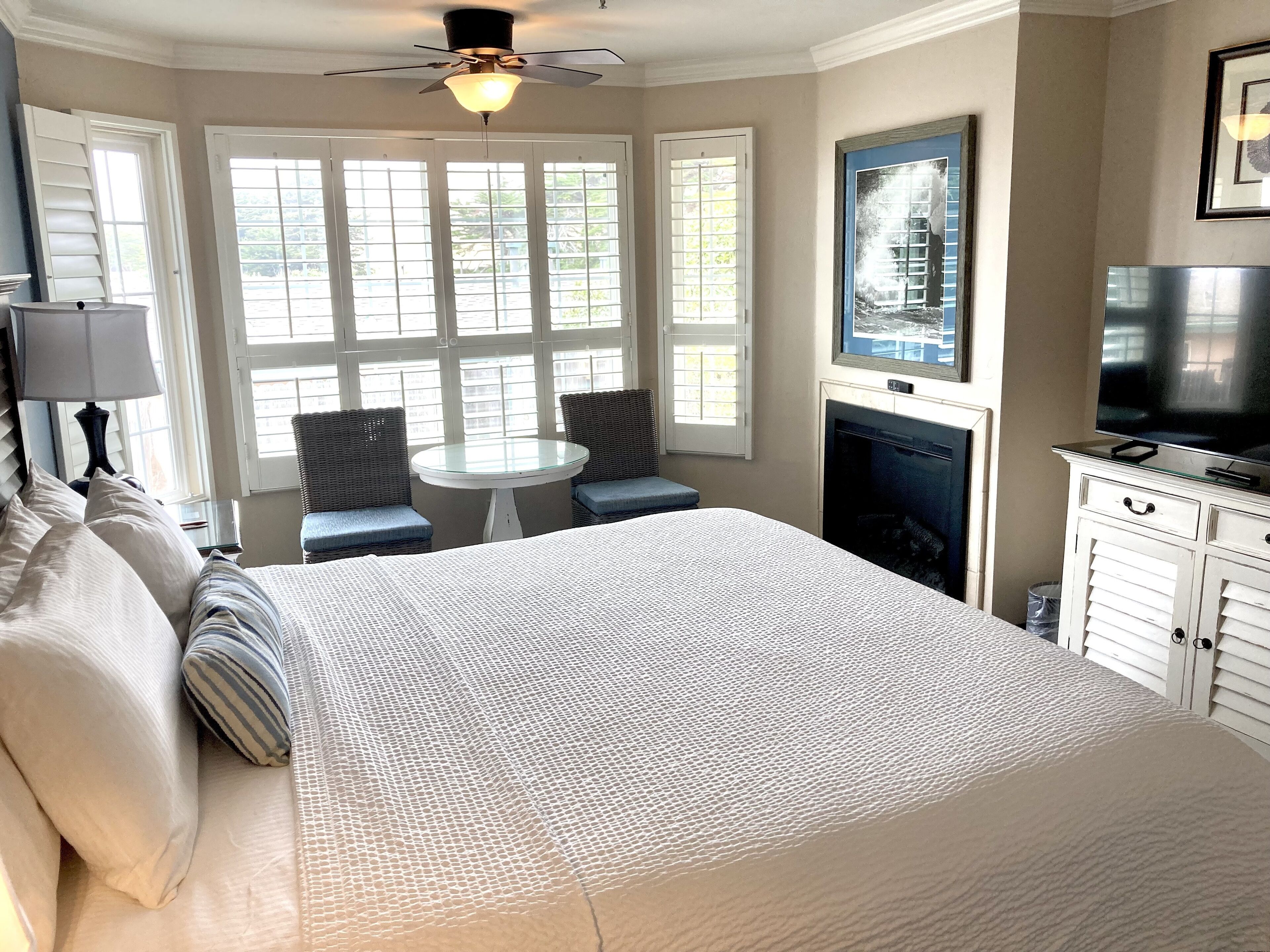 A bedroom with a large bed, a small round table, two chairs, a television, and a fireplace.