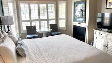 A bedroom with a large bed, a small round table, two chairs, a television, and a fireplace.