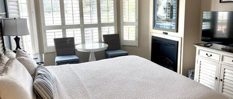A bedroom with a large bed, a small round table, two chairs, a television, and a fireplace.