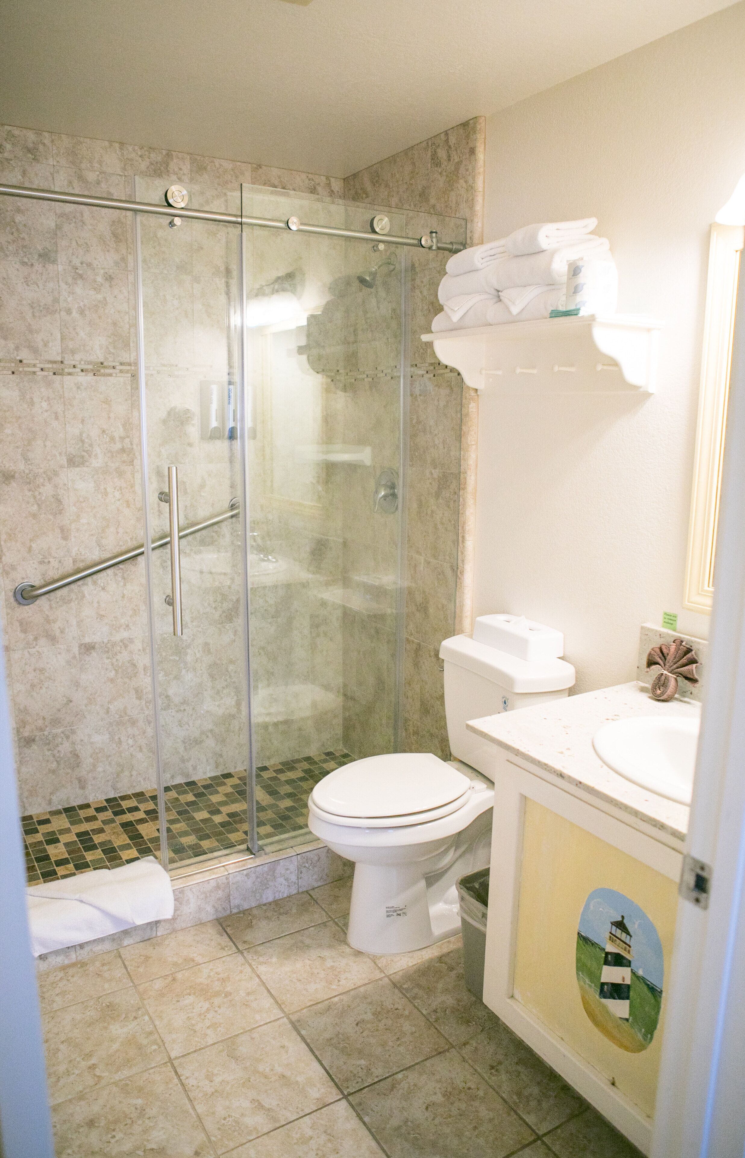 A bathroom with a glass shower enclosure, a toilet, and a sink with a towel rack.