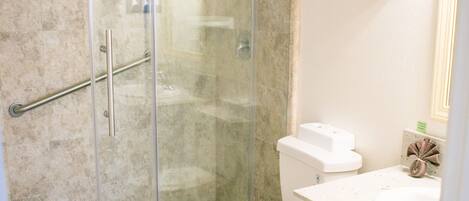 A bathroom with a glass shower enclosure, a toilet, and a sink with a towel rack.