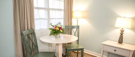 Una habitación con una mesa redonda, dos sillas, un pequeño mesita de noche y una lámpara.