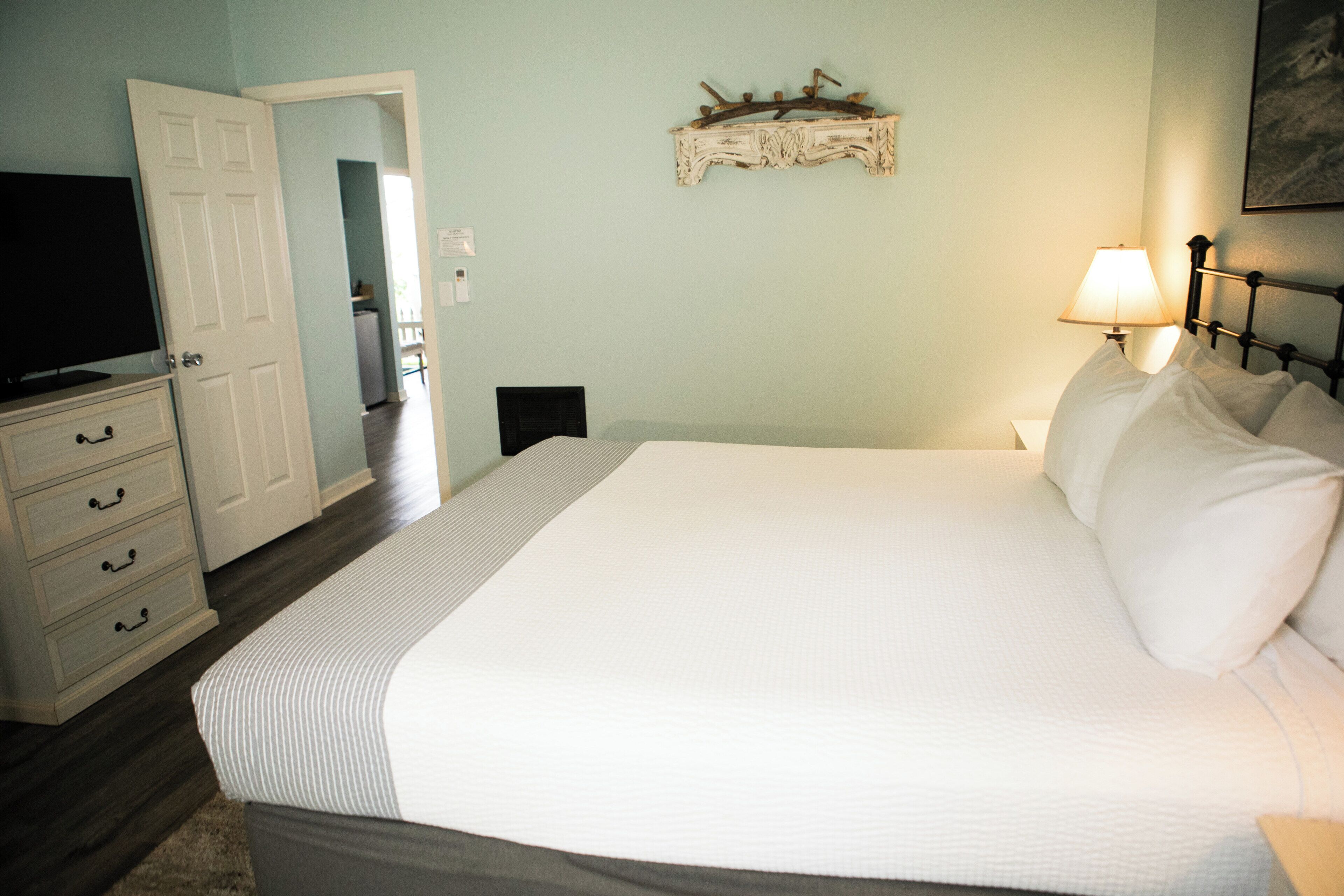 Un dormitorio con cama, cómoda, televisor y estante en la pared.