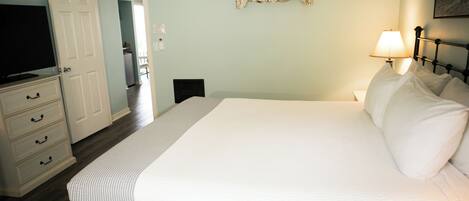 Un dormitorio con cama, cómoda, televisor y estante en la pared.