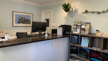 A reception desk with a computer, a framed picture, a welcome sign, and a display of local attractions.