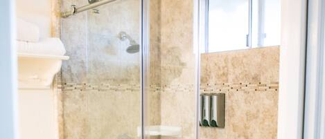A glass-enclosed shower stall with a handrail, a toilet, and a checkered floor pattern.