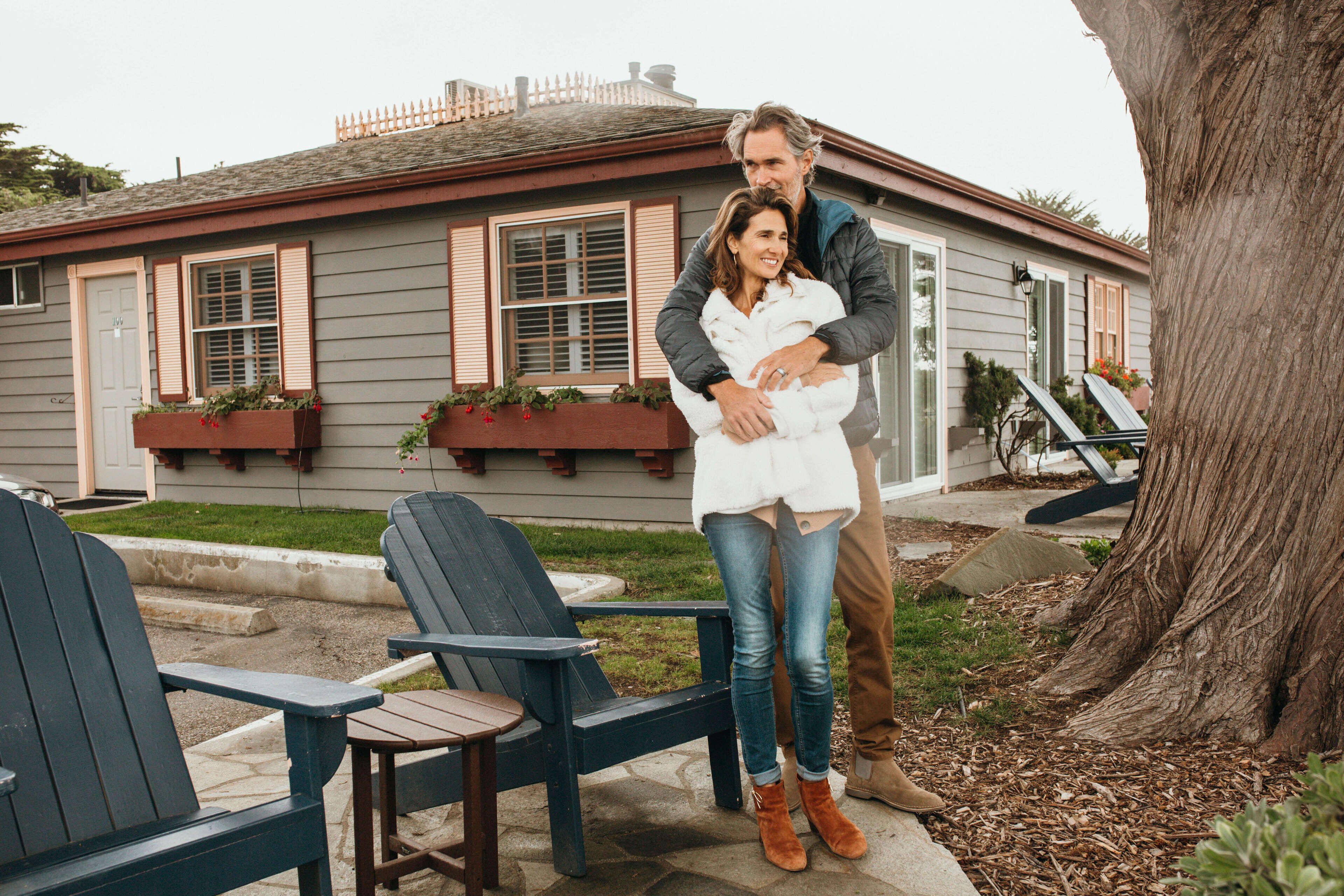 A house with a front porch, two Adirondack chairs, and a large tree.