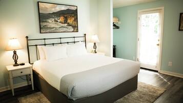 A bedroom with a bed, two bedside tables, a nightstand, a lamp, a painting, and a door.
