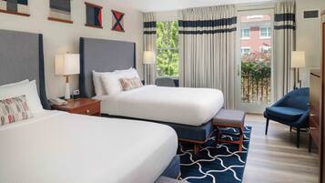 A hotel room with two beds, a desk, a chair, and a view of the outside.