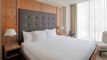 Quarto de hotel com uma cama grande, cabeceira de madeira, duas mesas de cabeceira com luminárias e uma cadeira.