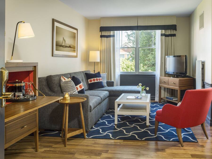 Una sala de estar con sofá, un sillón rojo, una mesita de centro, televisor y chimenea.
