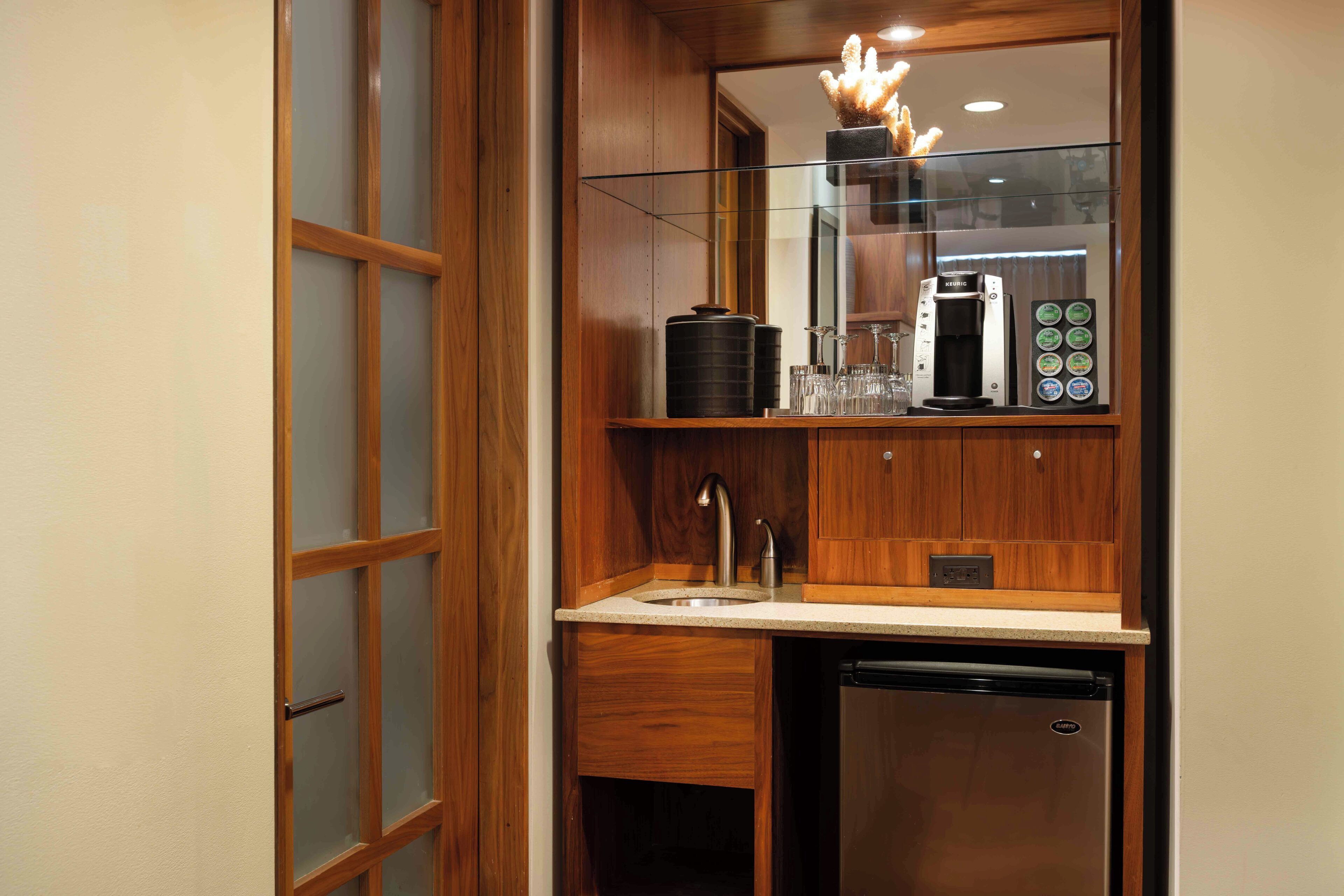 A compact kitchenette with a built-in dishwasher, a coffee maker, and a glass display cabinet.