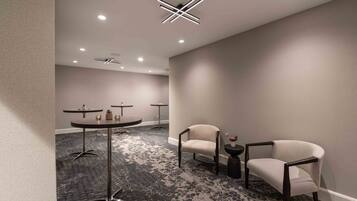 Un moderno vestíbulo de hotel con piso alfombrado, una mesa redonda con un florero, dos sillones y una lámpara en el techo.