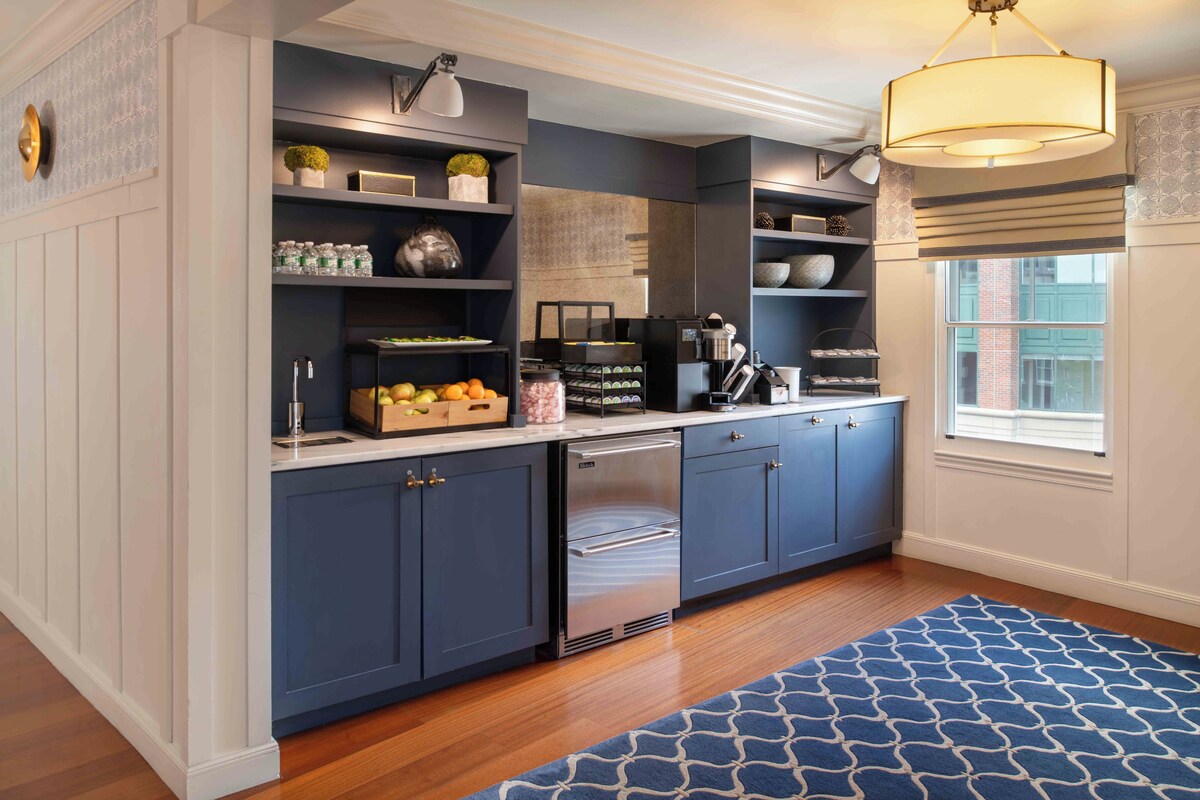 A modern kitchen with dark blue cabinets, a stainless steel refrigerator, and a blue patterned rug.