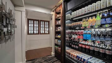 A hotel room with a minibar stocked with beverages, a wooden cabinet, and a window with blinds.