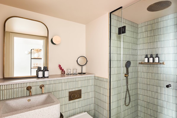 Un baño con una bañera independiente, una ducha con cabezal de ducha manual, un lavamanos con espejo y un estante con artículos de tocador.