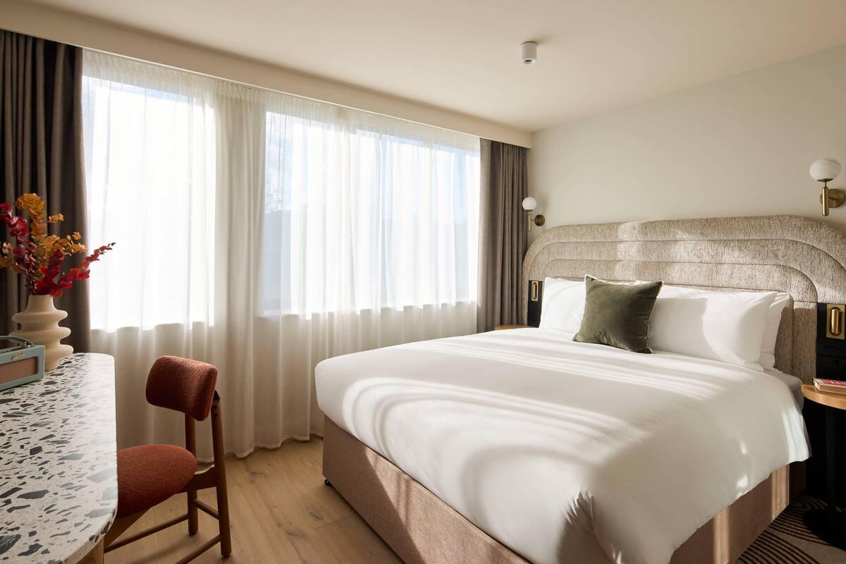 A hotel room with a large bed, a dining table, a chair, and a vase with flowers.