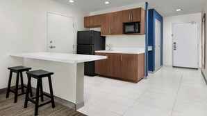 A modern kitchen with white countertops, wooden cabinets, a black refrigerator, and two black stools. - Holiday Inn Express Hotel & Suites Marina - State Beach Area by IHG (Marina)