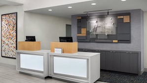 A reception area with a modern design, featuring a reception desk with a digital display, a wall-mounted information board, and a patterned artwork on the wall. - Holiday Inn Express Hotel & Suites Marina - State Beach Area by IHG (Marina)