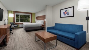 A hotel room with a bed, a blue sofa, a wooden desk, a chair, and a framed picture on the wall. - Holiday Inn Express Hotel & Suites Marina - State Beach Area by IHG (Marina)