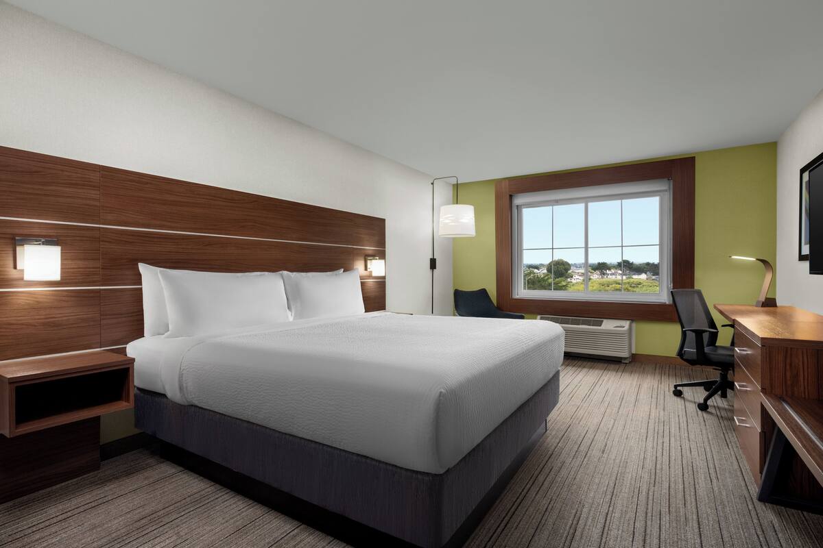 A hotel room with a large bed, a desk, a chair, and a window with a view.