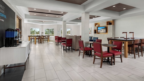 A modern cafe with a long counter, red chairs, and a large window. - Holiday Inn Express Hotel & Suites Marina - State Beach Area by IHG (Marina)
