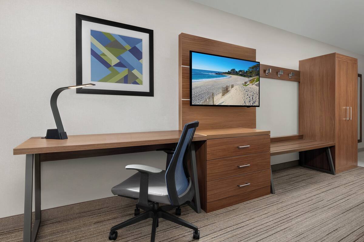 A modern office space with a desk, chair, and a mounted TV displaying a beach scene.