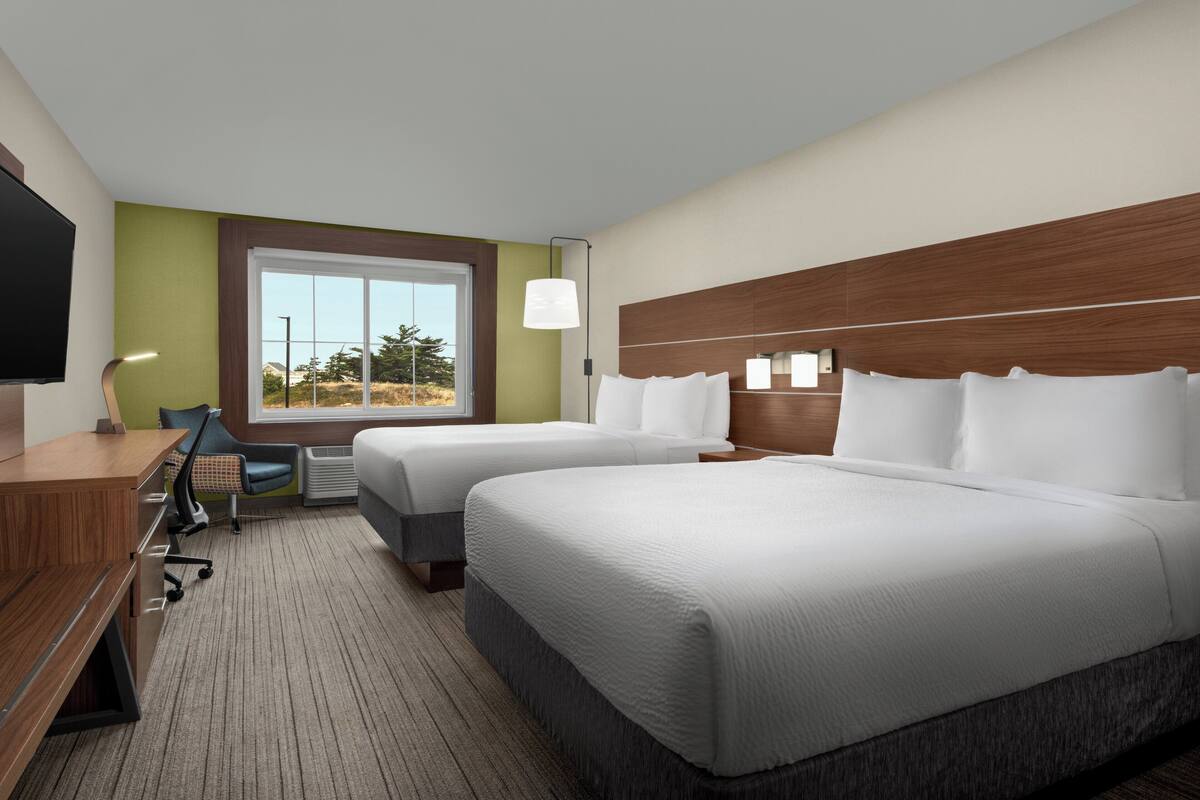 A hotel room with two beds, a desk, a chair, a TV, and a window with a view of trees.