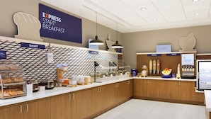 Un área de desayuno con un cartel que anuncia el desayuno Express Start, una sección de panadería y un mostrador con diferentes opciones de comida y una pantalla digital.