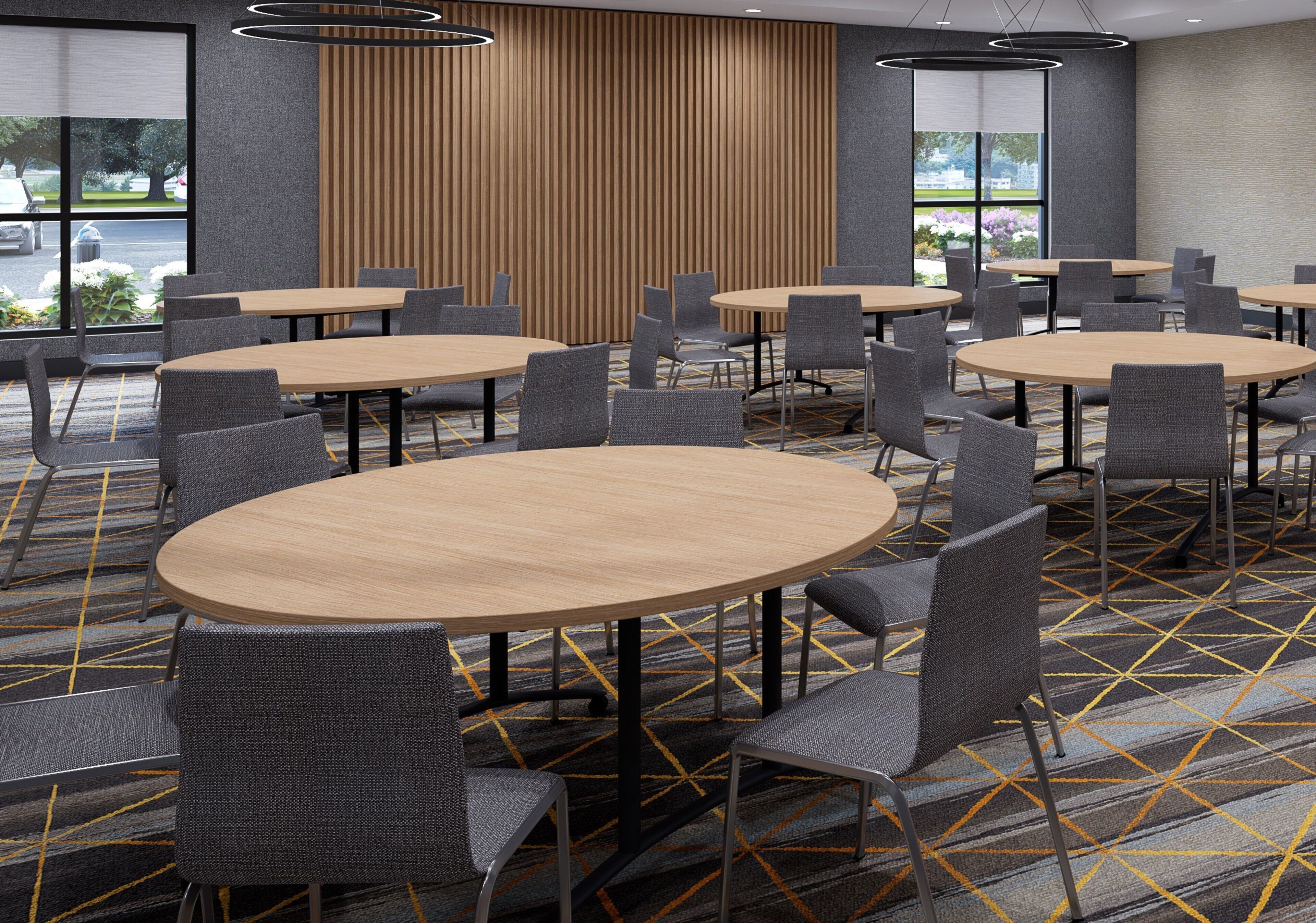 Een vergaderruimte met meerdere ronde tafels en stoelen, een kamerbreed tapijt met patroon en grote ramen met uitzicht op het omliggende landschap.