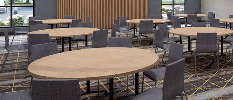 Een vergaderruimte met meerdere ronde tafels en stoelen, een kamerbreed tapijt met patroon en grote ramen met uitzicht op het omliggende landschap.