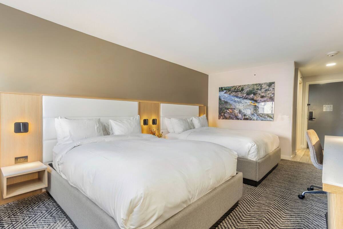 A hotel room with two beds, a desk, a chair, and a painting on the wall.