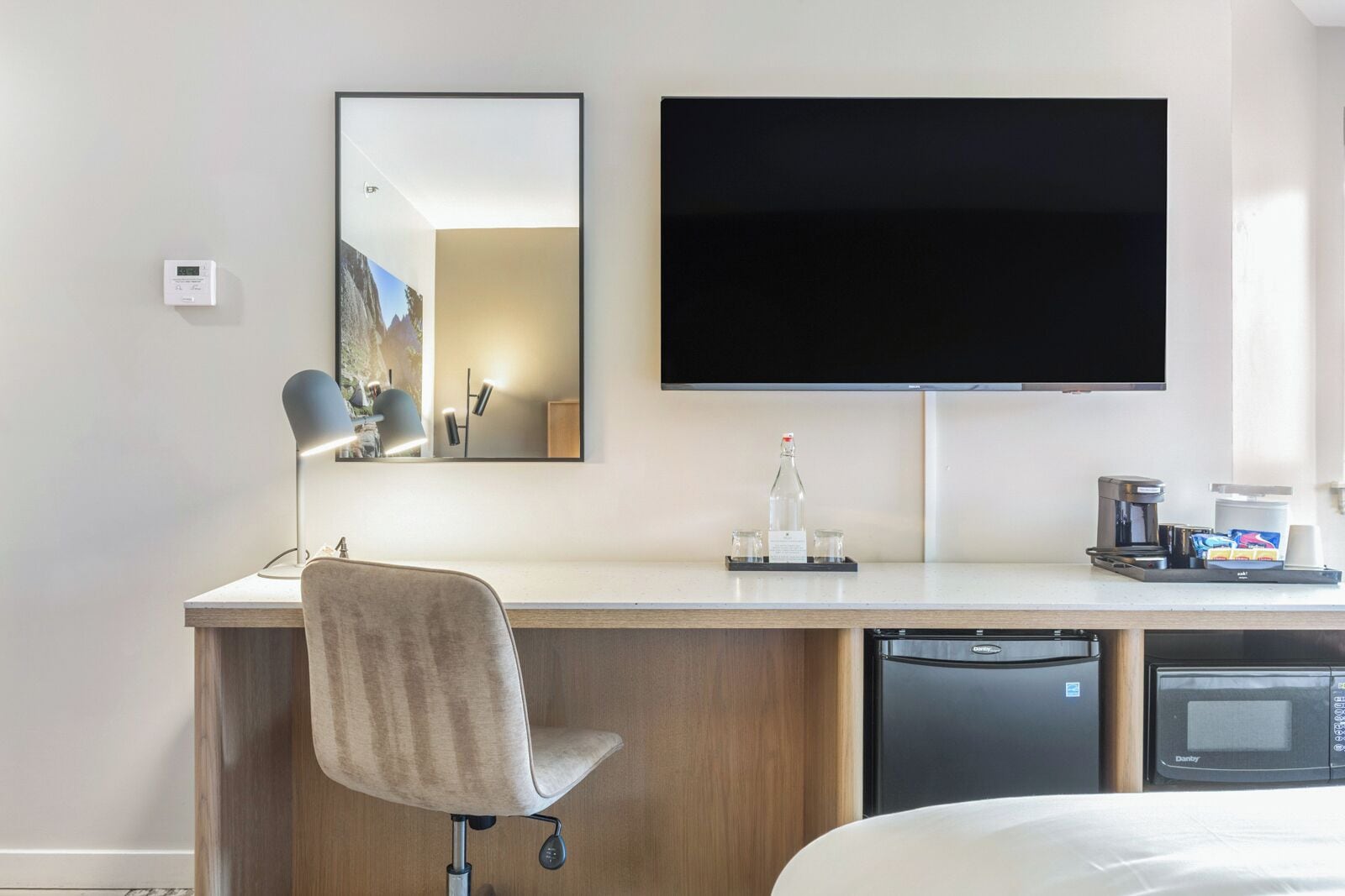 Habitació d'hotel amb llit, escriptori amb cadira, televisió de pantalla plana, cafetera, microones i rentaplats.
