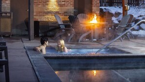 A heated outdoor pool area with lounge chairs and a fire feature, surrounded by a brick building and snow on the roof. - The Inn at Riverwalk (Edwards)