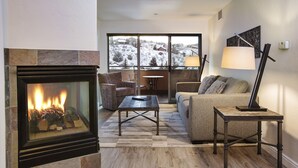 A cozy living room with a fireplace, a sofa, a coffee table, and a lamp. - The Inn at Riverwalk (Edwards)