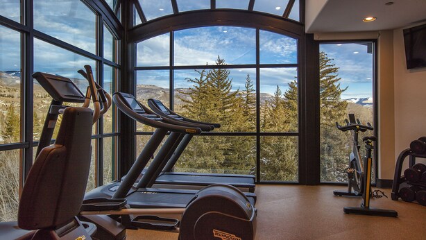 A gym with treadmills, stationary bikes, and dumbbells, featuring large windows with a mountain view. - The Inn at Riverwalk (Edwards)