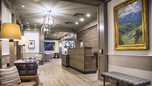 A hotel lobby with a wooden reception desk, a bench, and a large painting on the wall. - The Inn at Riverwalk (Edwards)
