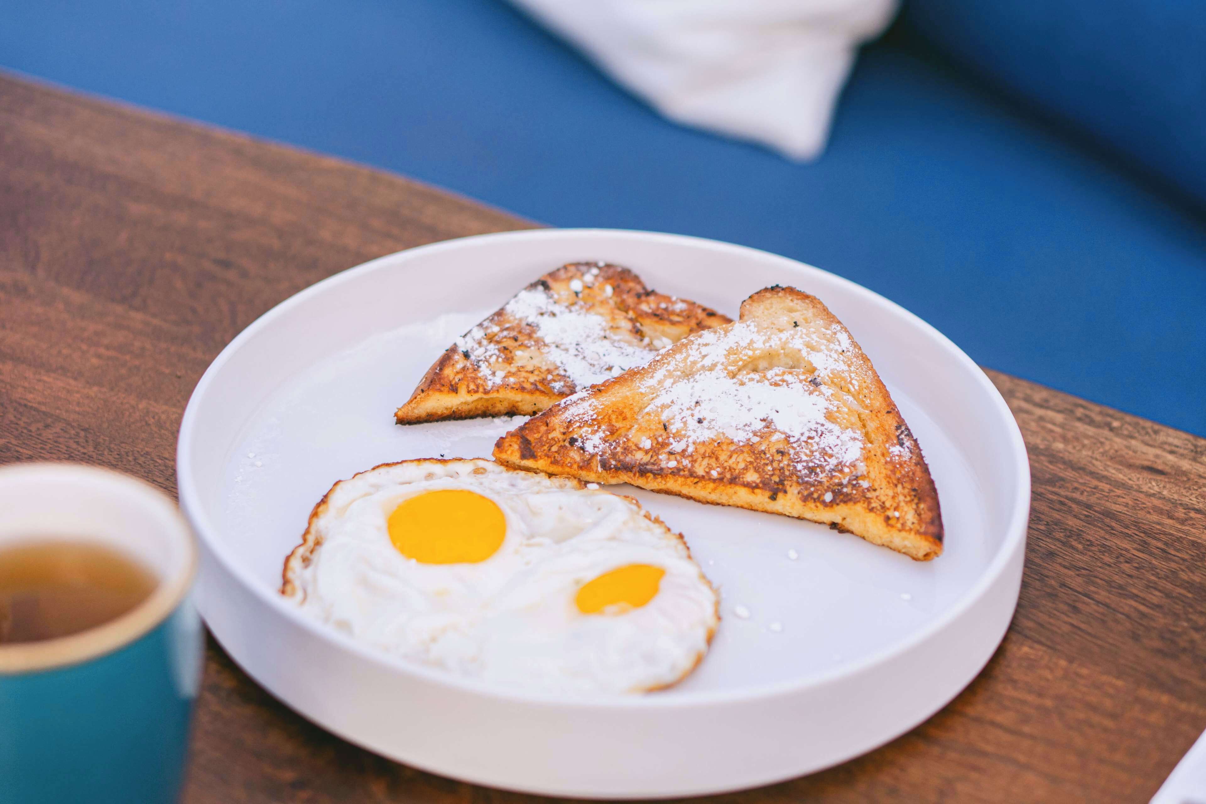 A plate with two pieces of toasted bread and two fried eggs on a wooden table.