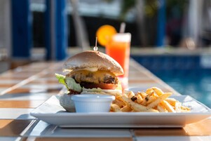 A meal consisting of a burger, fries, and a drink by a poolside.