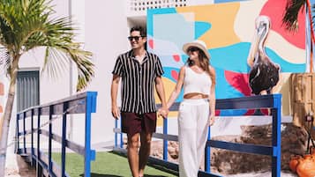 A couple walking on a pathway with a white building and a colorful mural in the background.