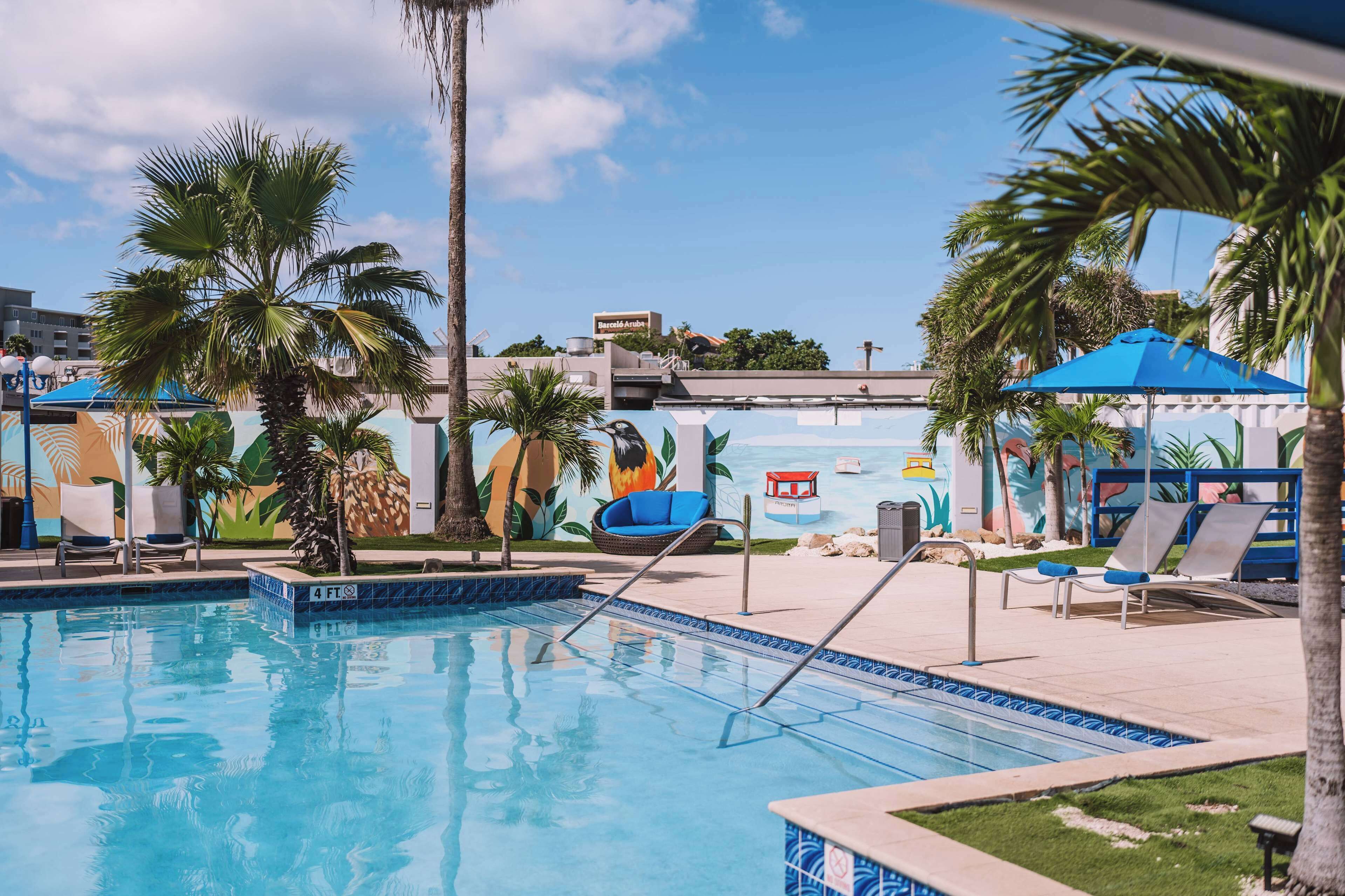 Una piscina con sillones de descanso y un mural al fondo.